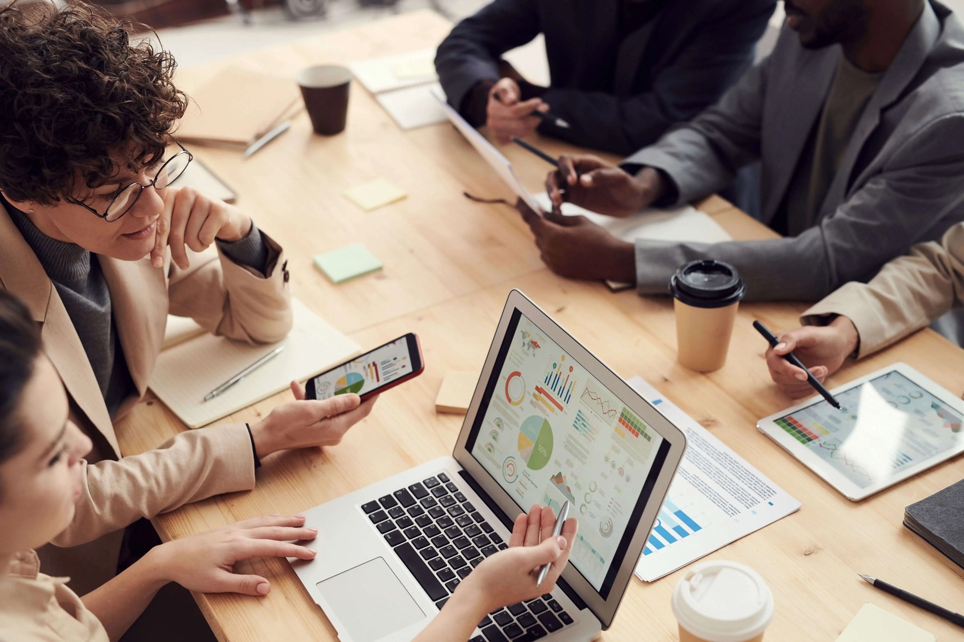 Team am Besprechungstisch mit Laptop, Tablet und ausgedruckten Auswertungen