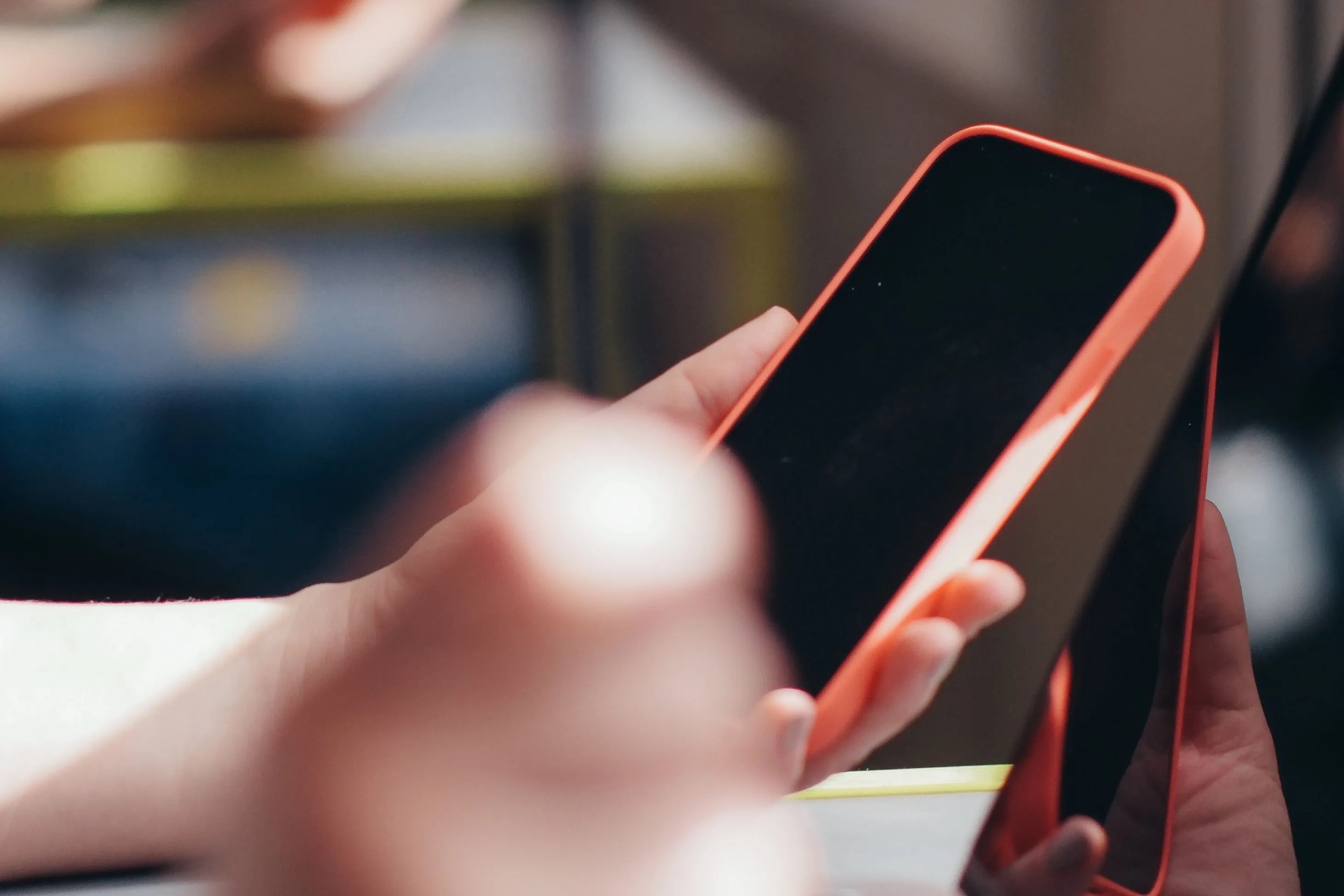 Hände mit einem Smartphone vor einem aufgeklappten Laptop