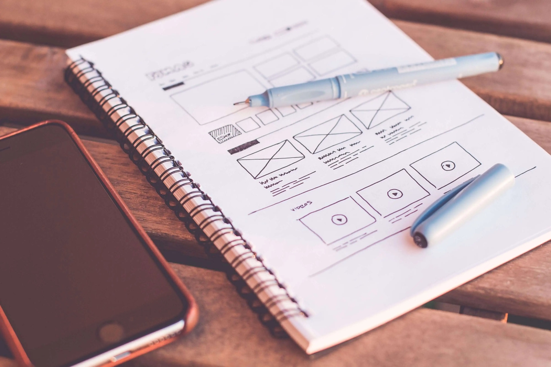 Handgezeichneter Entwurf einer Webseite in einem Notizbuch, daneben Stift und Smartphone